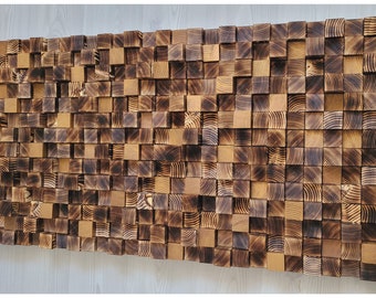 Op de afbeelding: Een rechthoekig wandkunstwerk bestaande uit talloze kleine, vierkante houten blokjes met variërende dieptes. De blokjes vertonen een mix van natuurlijke lichtbruine houtnerven en geblakerde, donkerbruine oppervlakken, wat een textuurrijk 3D-raster vormt.