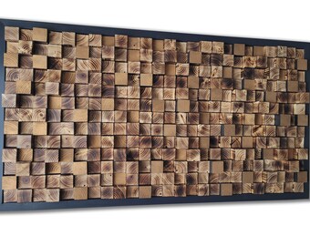 Op de afbeelding: Een rechthoekig wandkunstwerk bestaande uit talloze kleine, vierkante houten blokjes met variërende dieptes en bruintinten, met zichtbare houtnerven en geblakerde randen, gevat in een dun, massief zwart rechthoekig frame.