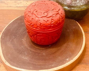 May include: A red carved wooden box with intricate floral designs and Chinese characters. The box is sitting on a wooden base.