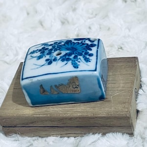Puede incluir: Un pequeño quemador de incienso cuadrado de porcelana azul y blanco con un diseño floral. El quemador está sentado sobre una base de madera.