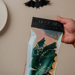 May include: A clear plastic bag with a black header card that reads "SAD GIRL CRAFT" and contains a set of black paper bats with white twine.