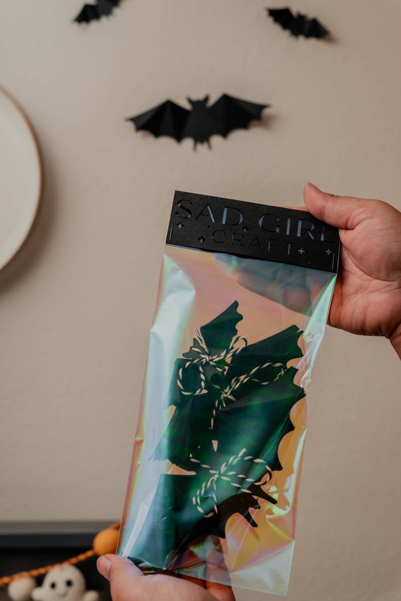 May include: A clear plastic bag with a black header card that reads "SAD GIRL CRAFT" and contains a set of black paper bats with white twine.