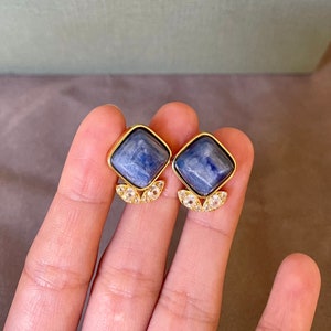 Puede incluir: Un par de pendientes de oro con piedras cuadradas de piedra preciosa azul y detalles de cristal transparente.