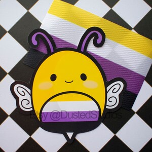 May include: A yellow and black bee with purple wings and a white, yellow, and purple stripe across its body. The bee is on a black and white checkered background.