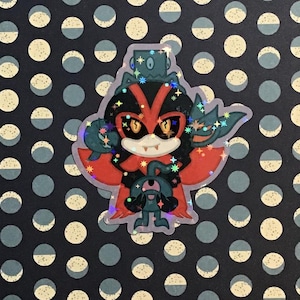 May include: A holographic sticker featuring a cartoon character with a red and black color scheme. The character has a V-shaped design on its face, with yellow eyes and a small, white-toothed grin. The sticker has a blue and green color scheme and is decorated with stars.