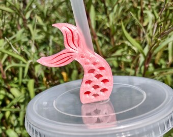 May include: Pink mermaid tail straw topper for a reusable cup or tumbler. The topper is made of plastic and has a detailed mermaid tail design with scales.