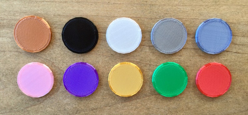 May include: Ten round, flat, plastic discs in various colors, including brown, black, white, gray, light blue, pink, purple, gold, green, and red.