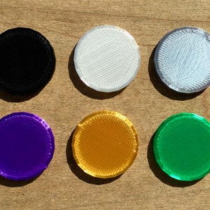 May include: Ten round, flat, plastic discs in various colors, including brown, black, white, light blue, pink, purple, gold, green, and red.