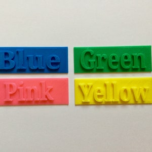 May include: Four rectangular blocks of color, each with a different color and the word for that color printed on it. The colors are blue, green, pink, and yellow.