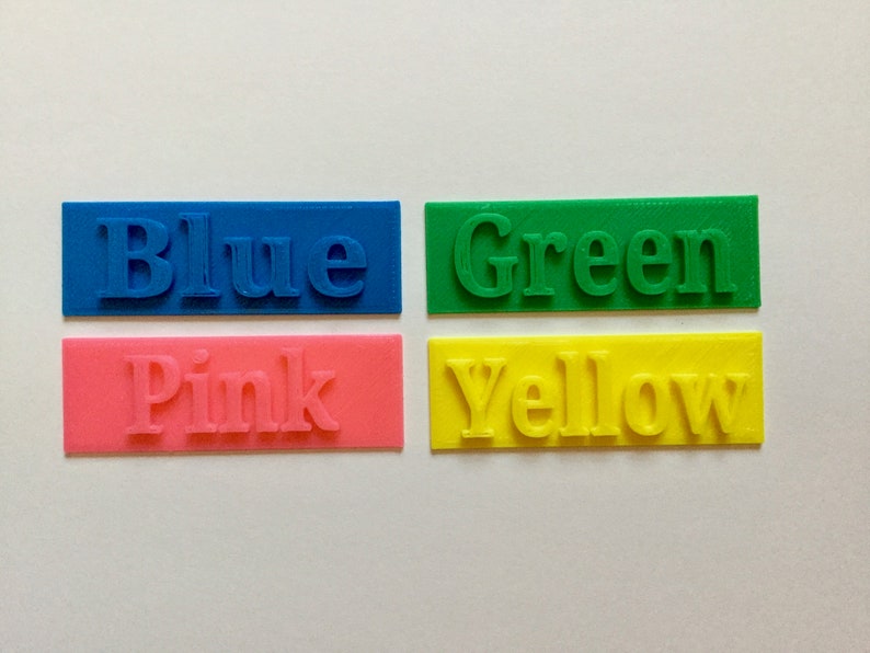 May include: Four rectangular blocks of color, each with a different color and the word for that color printed on it. The colors are blue, green, pink, and yellow.