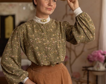 May include: A long-sleeved olive green blouse with a small floral pattern, a high white lace collar with a gold brooch, and a brown skirt. The outfit is paired with a straw boater hat featuring a brown ribbon band and white lace cuffs.