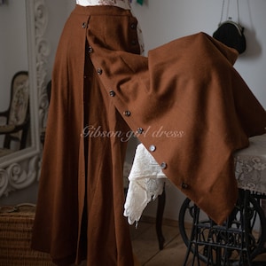 May include: A long, brown skirt with button detailing. The skirt is displayed on a mannequin and features a split front design. The text "Gibson girl dress" is visible on the skirt.