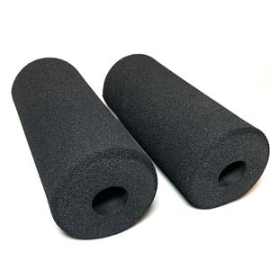 Könnte beinhalten: Zwei schwarze zylindrische Schaumstoffgriffe mit einem Loch an einem Ende. Die Griffe bestehen aus einem strukturierten Material und sind für die Verwendung an einem Fahrrad oder anderen Geräten konzipiert.