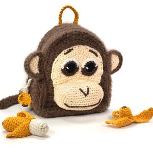 May include: A brown crocheted monkey backpack with big eyes and a smiling mouth. The backpack has a furry texture and comes with two small crocheted bananas.