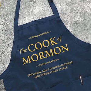 May include: Navy blue apron with the text "The COOK of MORMON" in gold lettering. The apron also features the text "THIS MEAL AIN'T GONNA NOURISH AND STRENGTHEN ITSELF". The apron has a pocket and a neck strap.