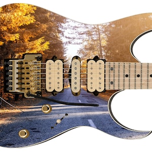 May include: A black electric guitar with a custom design featuring a scenic road through a forest with golden trees. The guitar has a white body and a black pickguard. The guitar has a maple fretboard and a rosewood body.