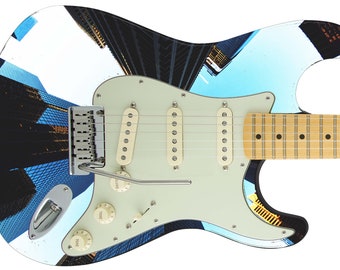 May include: A white electric guitar with a blue and black cityscape design. The guitar has a white pickguard, three knobs, and a chrome bridge.
