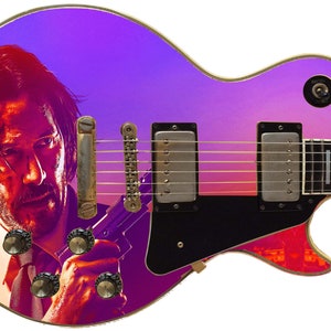 May include: A purple and pink electric guitar with a graphic of a man's face on the body. The guitar has a black pickguard and a gold bridge.