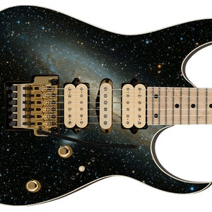 May include: Electric guitar with a galaxy design. The body is black with a swirling nebula pattern. It has gold hardware, including the bridge and tuning pegs. The fretboard is light-colored with black inlays.