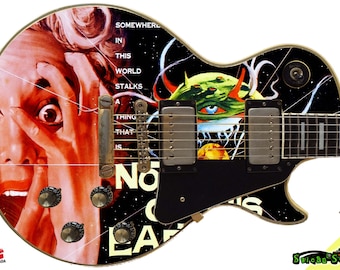 May include: A black electric guitar with a custom design featuring a woman's face with a shocked expression, a creature with a large eye, and the text "Somewhere in this world stalks a thing that is... No One On Earth".
