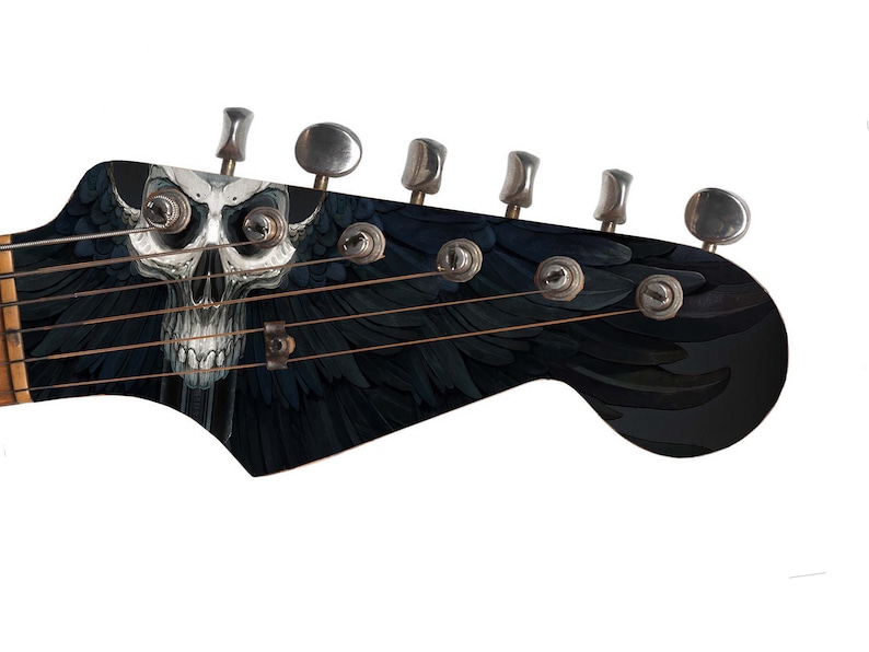 Pu&ograve; includere: Una paletta di chitarra elettrica nera con un design a forma di teschio e ali. La chitarra ha sei meccaniche e una finitura nera.