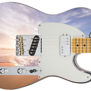 May include: A white electric guitar with a sunset and beach scene printed on the body. The guitar has a white pickguard, gold hardware, and a maple fretboard.