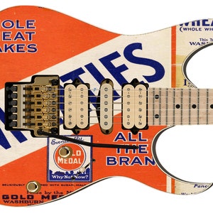 May include: A white, blue and orange electric guitar with a vintage cereal box design. The guitar has a  "Wheatles" logo and the text "Whole Wheat Flakes" and "All the Bran".