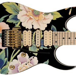 May include: Black electric guitar with a floral design featuring pink, white, and green flowers. The guitar has a gold-colored bridge and hardware.