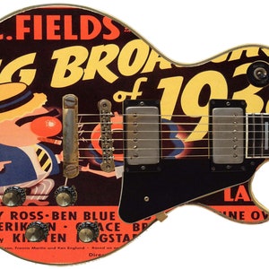 Peut inclure: Une guitare électrique noire et dorée avec un design d'affiche vintage représentant un homme de dessin animé portant un chapeau et le texte "The Big Broadcast of 1938".