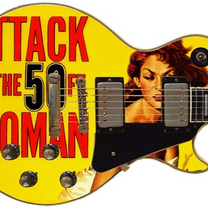 May include: A yellow electric guitar with a black pickguard. The guitar is decorated with a vintage movie poster for "Attack of the 50 Foot Woman".