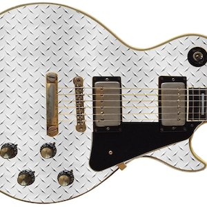 May include: A white electric guitar with a diamond plate pattern. The guitar has a black pickguard and gold hardware.