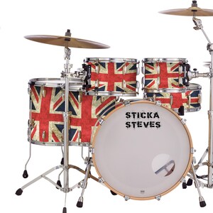 Puede incluir: Un juego de batería completo con diseño de la bandera del Reino Unido en los parches. El conjunto incluye bombo, caja y varios tom-toms, además de platillos y soportes. La caja presenta el texto "STICKA STEVES".
