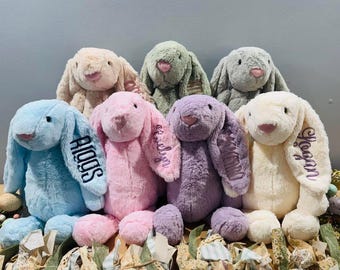 May include: Seven plush bunny toys in various colors, including blue, pink, purple, cream, and green. Each bunny has a different name embroidered on its ear, including "Logan", "Audrey", "Addison", "Naomi", "Evelyn", and "Aiden".