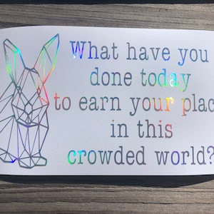 May include: A white sticker with a geometric rabbit design and the text "What have you done today to earn your place in this crowded world?"