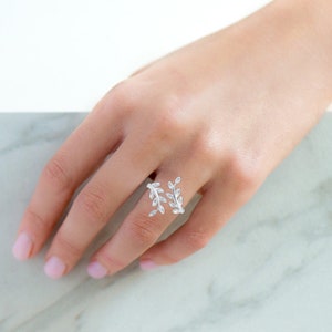 May include: A silver ring with a delicate design of two intertwining branches with leaves. The ring is adjustable and can be worn on any finger.