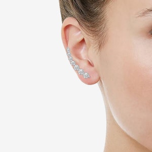 May include: A silver ear cuff with a row of clear cubic zirconia stones. The cuff is curved and wraps around the ear.
