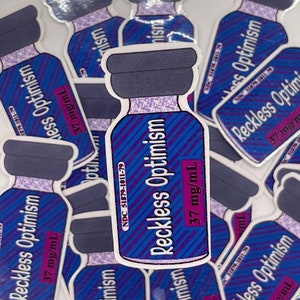 May include: A sticker featuring a blue and purple vial labeled "Reckless Optimism." The vial has a dark purple cap and contains the text "37 mg/mL" and "NDC 51879-1011-79."