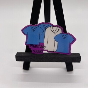 Peut inclure: Un autocollant violet avec trois personnages de dessin anim&eacute; portant des blouses et une blouse blanche. Le texte "Pharmacy Squad" est imprim&eacute; sur l'autocollant.