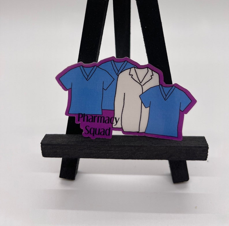 Peut inclure: Un autocollant violet avec trois personnages de dessin anim&eacute; portant des blouses et une blouse blanche. Le texte "Pharmacy Squad" est imprim&eacute; sur l'autocollant.
