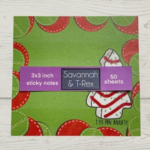 May include: A pack of 50 3x3 inch sticky notes featuring a green background with a red and white Christmas tree design. The text "Savannah & T-Rex" and "50 sheets" is printed on a purple label.