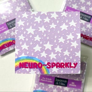 May include: A stack of 3x3 inch Post-it notes with a lavender background covered in white stars and small diamonds. The text "NEURO~SPARKLY" is displayed over a rainbow. The label reads "Savannah & T-Rex".