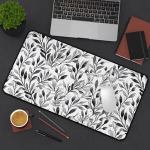 May include: A white desk mat with a black and white watercolor floral pattern. The mat is designed to protect a desk surface from scratches and wear.