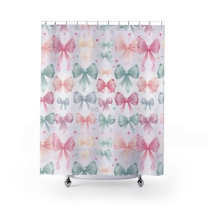 May include: A shower curtain featuring a repeating pattern of watercolor bows in pastel colors: pink, blue, green, and yellow. Small hearts are scattered throughout the design. The curtain is white with a subtle texture.