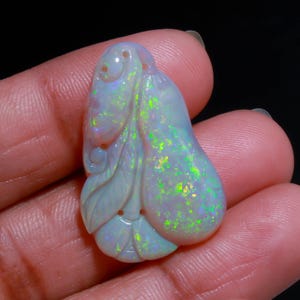 May include: A carved opal gemstone pendant featuring a pear-shaped body with an intricate leaf-like design on the side. The stone displays a milky white base color with vibrant flashes of neon green and subtle blue iridescent play-of-color.