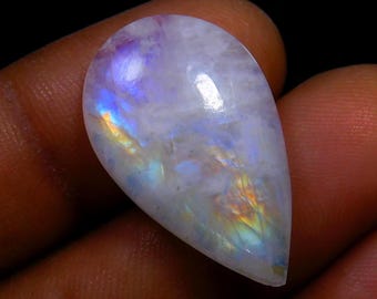 Könnte beinhalten: Ein tropfenförmiger, irisierender Mondstein-Cabochon mit einer weißen Basis und Schimmern in Blau, Lila und Orange.