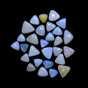 May include: A collection of triangular opals in various shades of white, blue, and yellow, arranged against a black background. The opals display iridescent flashes of color, showcasing their natural beauty. The gemstones vary in size and shape.