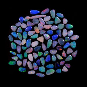 May include: A collection of polished opal gemstones in various shapes and sizes, including oval, teardrop, and irregular forms. The opals display a range of colors, including blue, green, red, and white, against a black background.