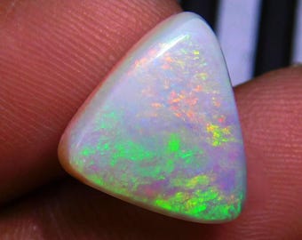 May include: A triangular-shaped opal gemstone featuring a smooth, polished surface with a milky white base color. The stone displays vibrant flashes of neon green, orange, and pink play-of-color across its entire face in a scattered pattern.