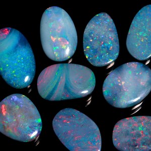 May include: A collection of polished opals with a variety of shapes and sizes. The opals display a range of colors, including blues, greens, and reds, with iridescent flashes. The gemstones are set against a black background.