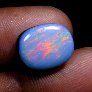 Puede incluir: Una piedra preciosa de ópalo ovalada azul con destellos iridiscentes de rosa, verde y naranja.